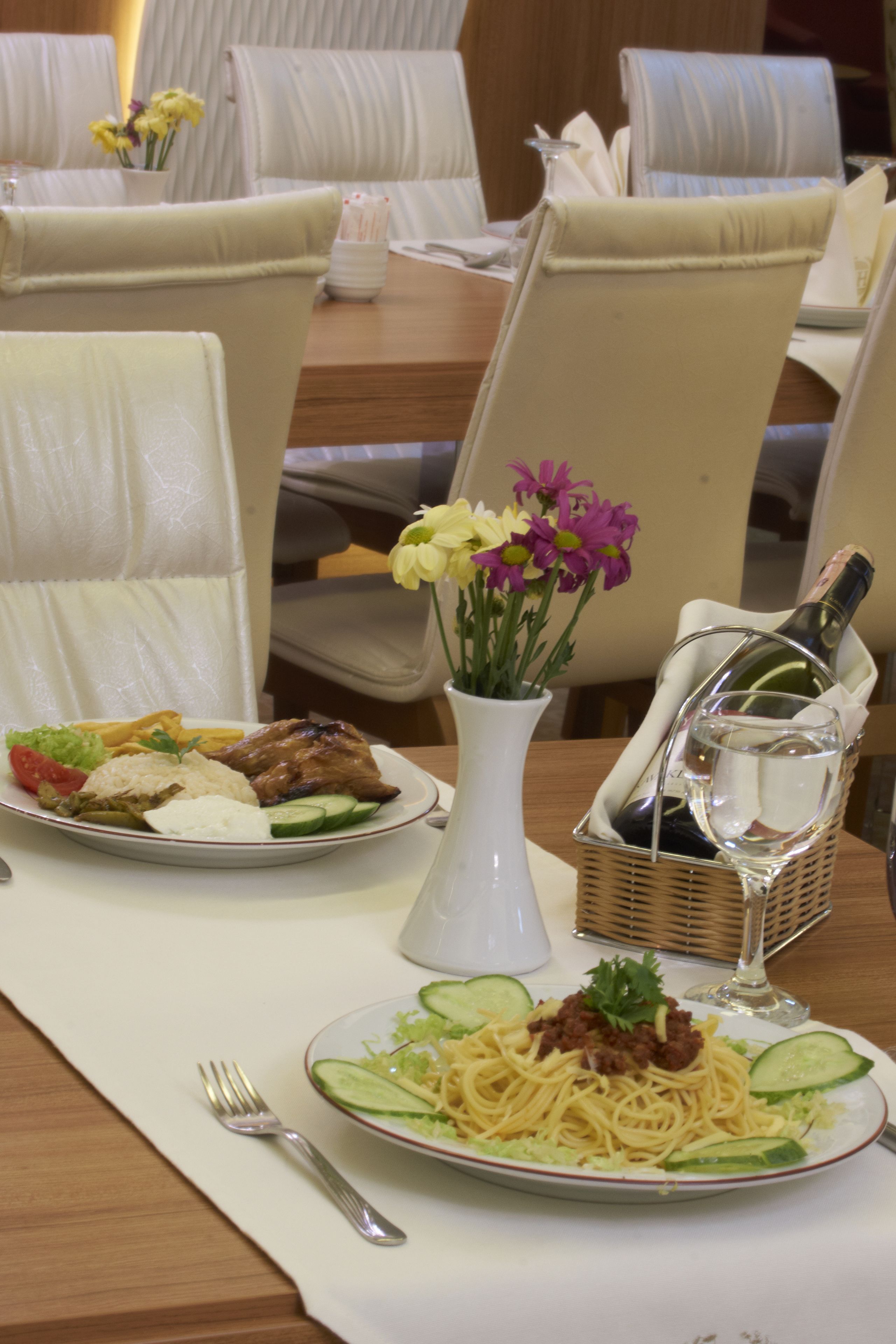 A dining table set with plates of food, a vase with flowers, and a bottle of water.