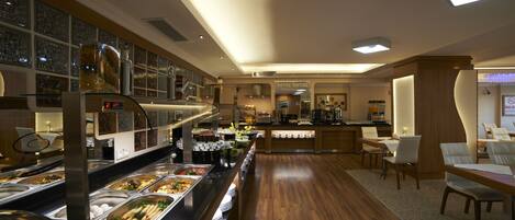 Un área de buffet con diferentes estaciones de comida y un espacio de comedor con mesas y sillas.
