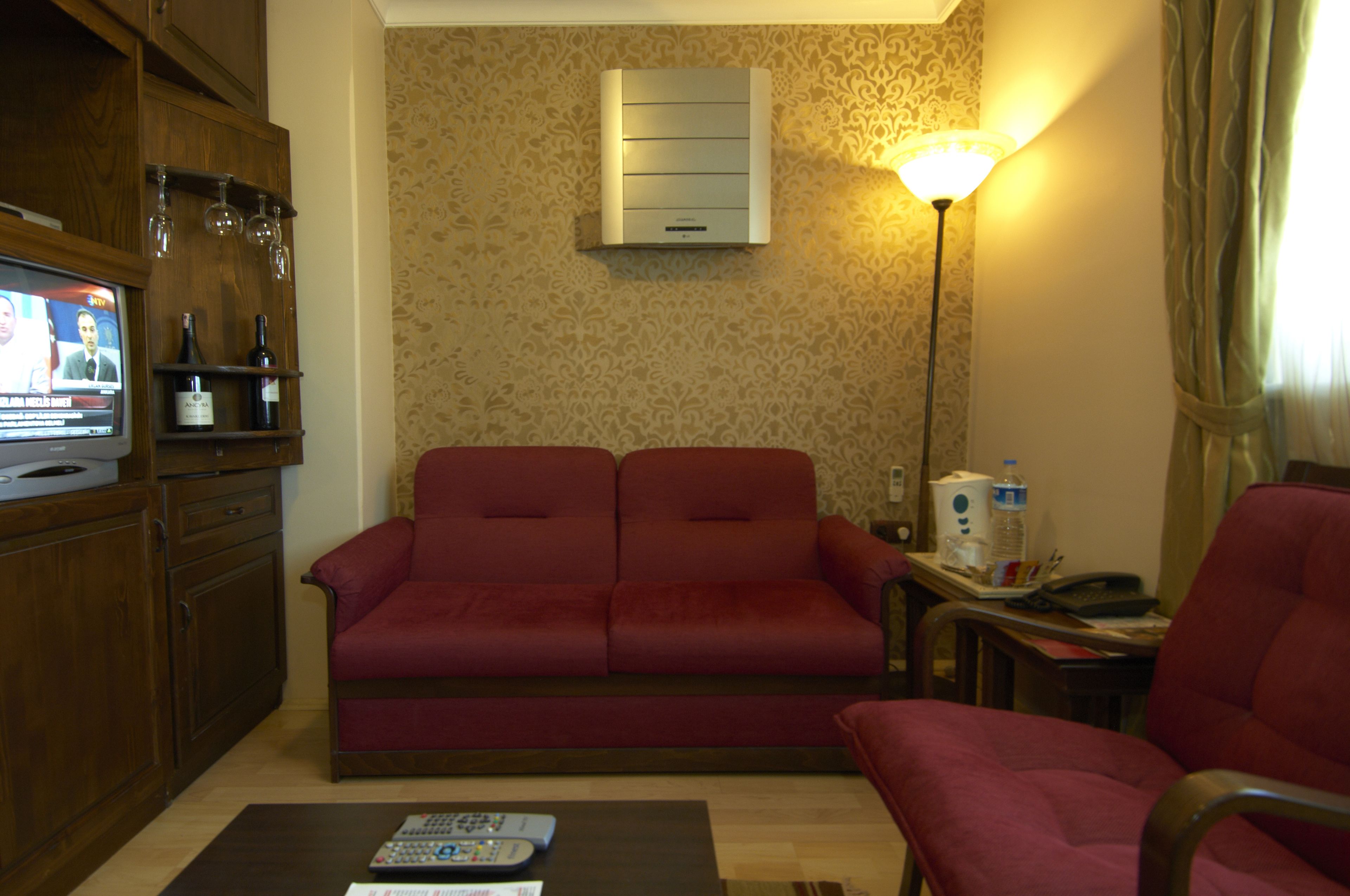 A living room with a red sofa, a wooden cabinet with wine glasses, a TV, and a lamp.