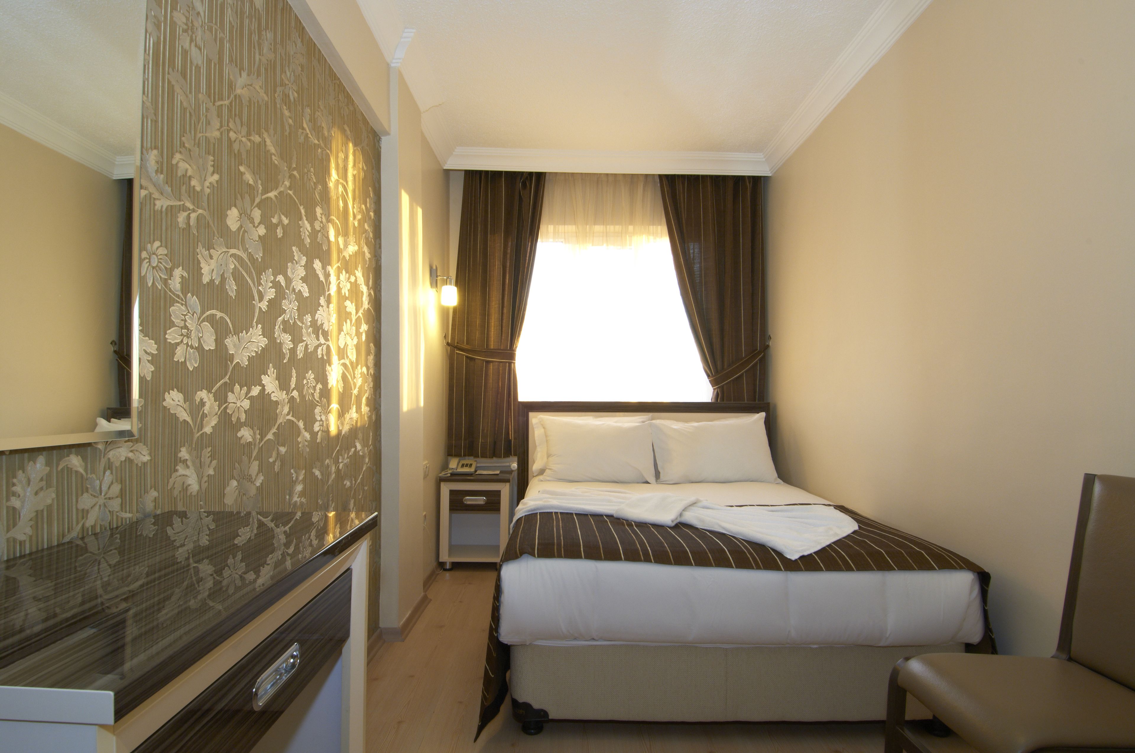 A hotel room with a bed, bedside table, lamp, and a view of the outdoors.