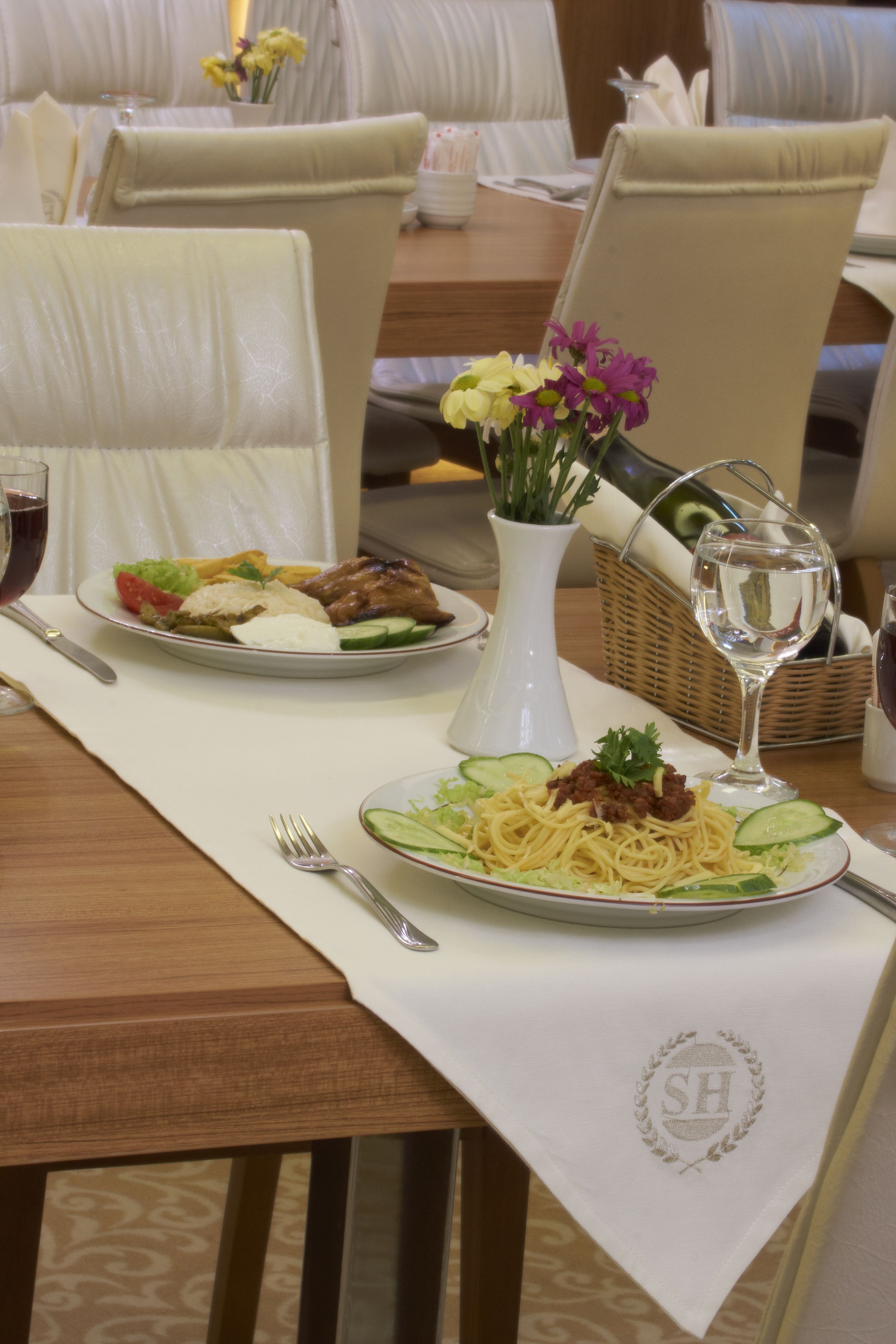 A dining table set with plates of food, a vase with flowers, and wine glasses.