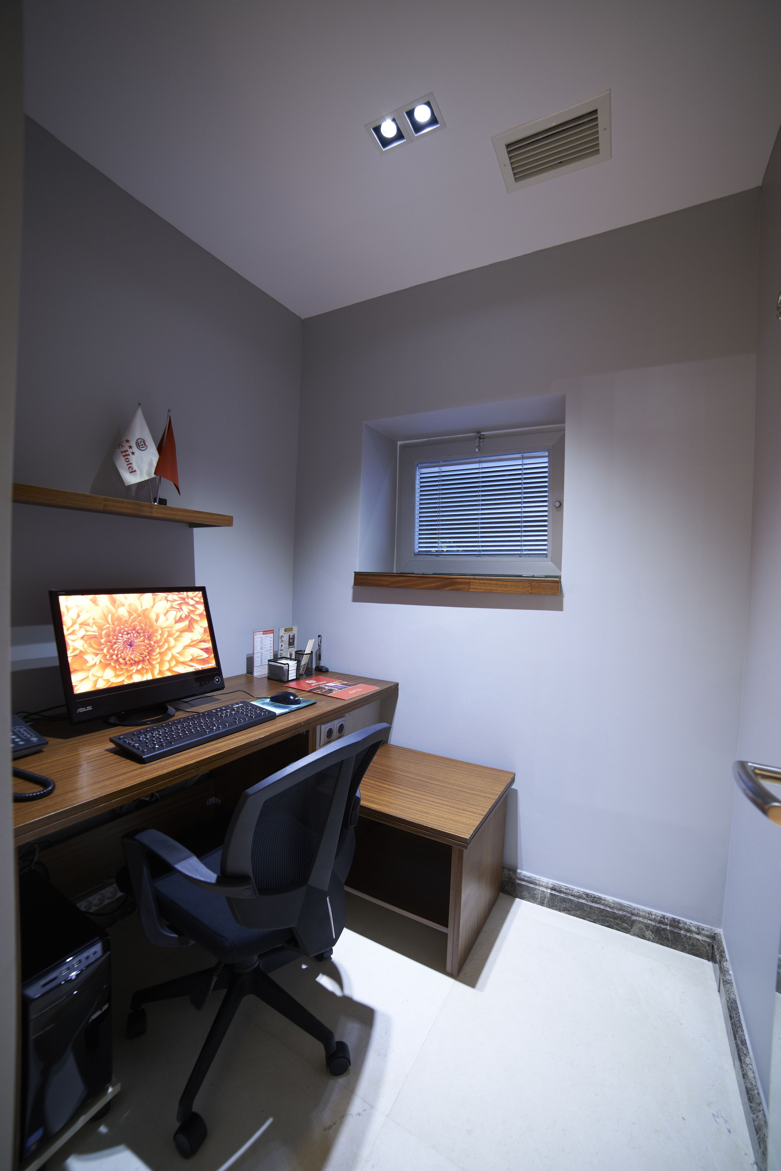 Un espacio de oficina pequeño y bien iluminado, con escritorio, computadora, silla y una ventana con persianas.
