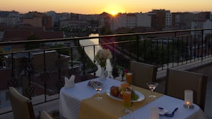 A dining table set for two with a view of the sunset over a river and cityscape. - Soyic Hotel (Eskisehir)