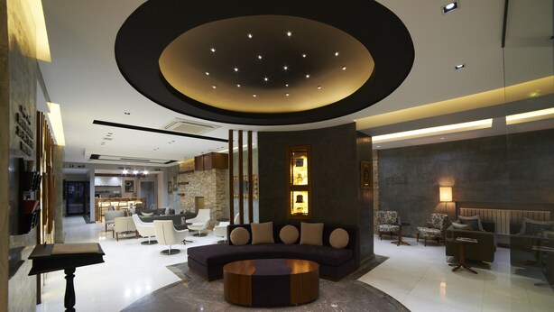 A modern lobby with a sectional sofa, round coffee table, and a circular ceiling feature. - Soyic Hotel (Eskisehir)