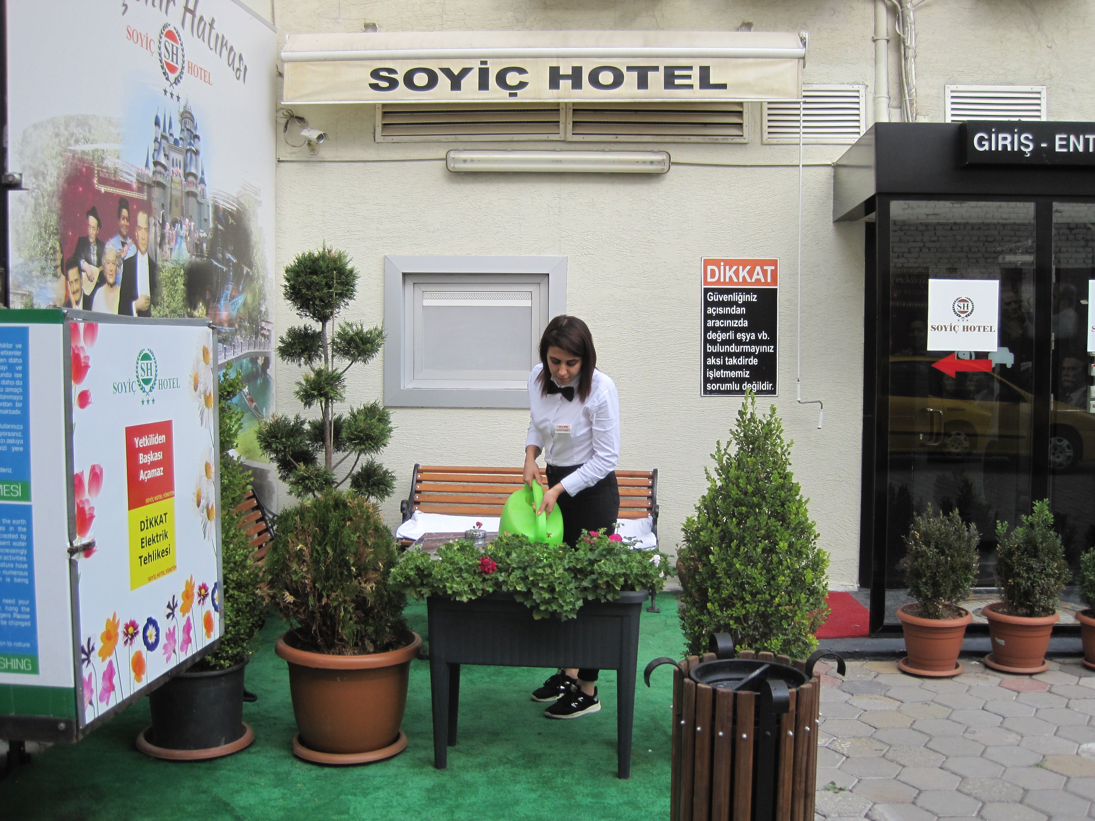 A hotel exterior with a sign for 'SOYIC HOTEL' and a 'DİKKAT' sign indicating a cautionary notice.