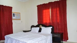 A bedroom with a bed, a nightstand, a wall-mounted air conditioner, and red curtains. -  Al Eairy Serviced Apartments Company is a one-person company 1 (Nairyah)