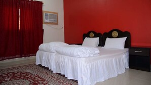 A room with a bed, red curtains, a patterned rug, and a wall-mounted air conditioner. -  Al Eairy Serviced Apartments Company is a one-person company 1 (Nairyah)