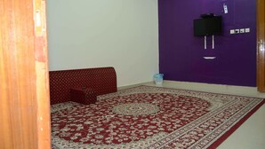 A room with a red patterned carpet, a red sofa, a purple wall, and a television mounted on the wall. -  Al Eairy Serviced Apartments Company is a one-person company 1 (Nairyah)