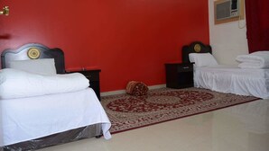 A room with two beds, a red wall, a patterned rug, and a small decorative item on the floor. -  Al Eairy Serviced Apartments Company is a one-person company 1 (Nairyah)