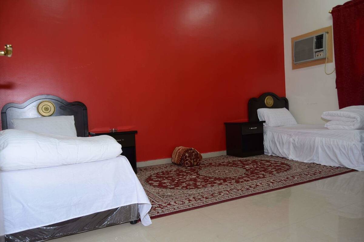 Una habitación con dos camas, una pared roja, un tapete estampado y un pequeño objeto decorativo en el suelo.