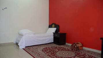 A single bed with white bedding, a nightstand, a red wall, and a patterned rug.