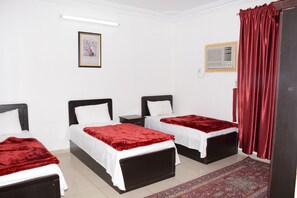 A room with two beds, each with a red blanket and white sheets, a small framed picture on the wall, and a red curtain on the window.