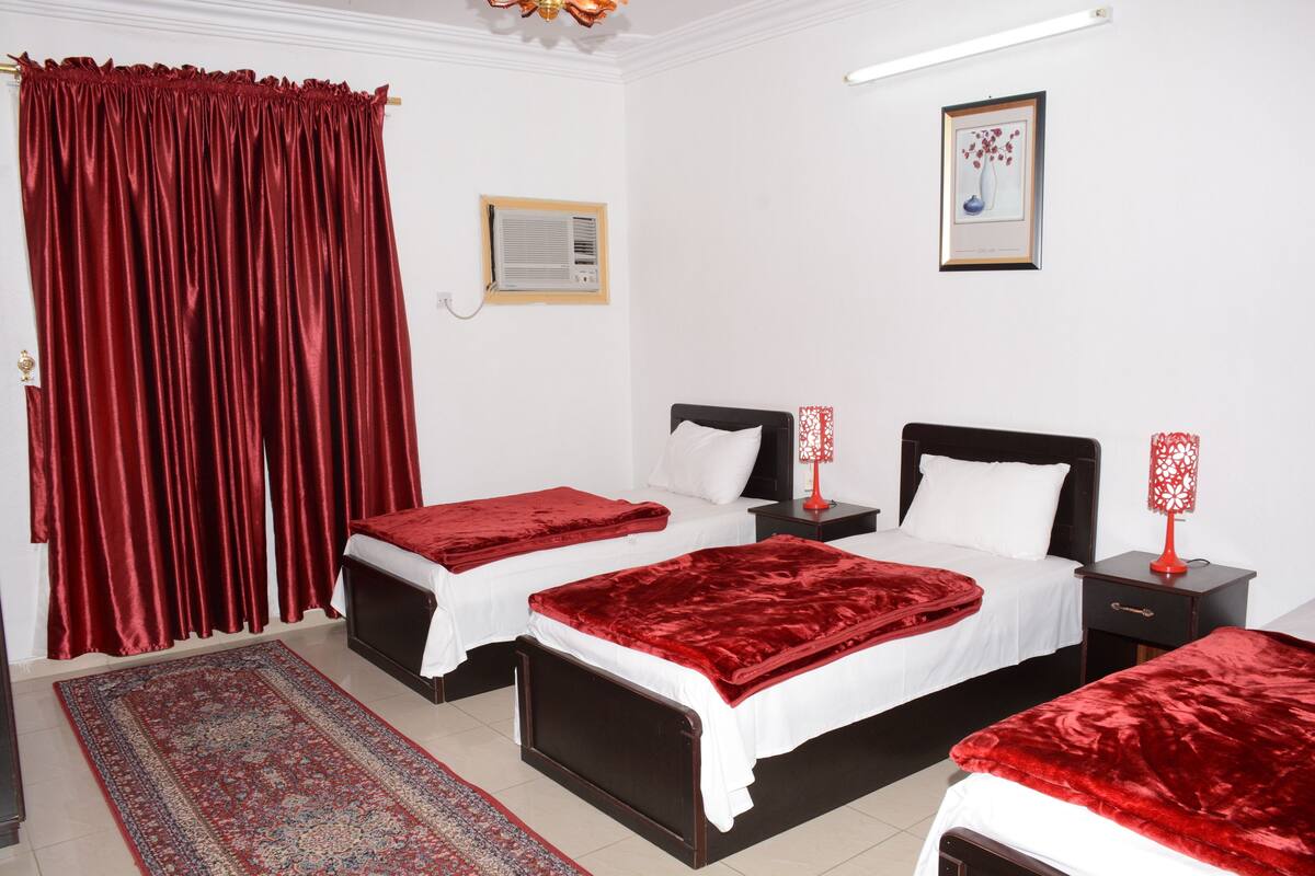 Une chambre d’hôtel avec deux lits, une literie rouge, un tapis à motifs, un rideau rouge, un tableau encadré au mur et une lampe rouge sur la table de chevet.