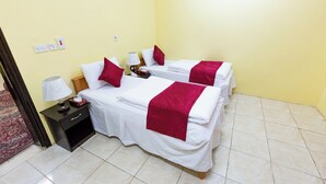 Habitació d'hotel amb dos llits, cada un amb roba de llit blanca i detalls vermells, una tauleta de nit amb una làmpada i un calaix petit.