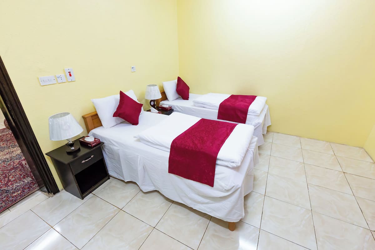 Une chambre d’hôtel avec deux lits, chacun agrémenté de draps blancs et de touches de couleur rouge, une table de chevet avec une lampe et un petit tiroir.