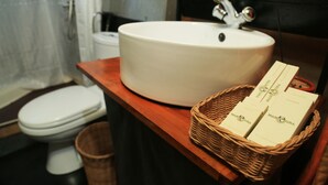 A bathroom with a white sink, a wooden countertop, and a wicker basket containing two boxes of shampoo. - Explorer by eco team -Dambana (Mahiyanganaya)