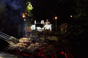 A grill with meat being cooked outdoors at night. - Explorer by eco team -Dambana (Mahiyanganaya)
