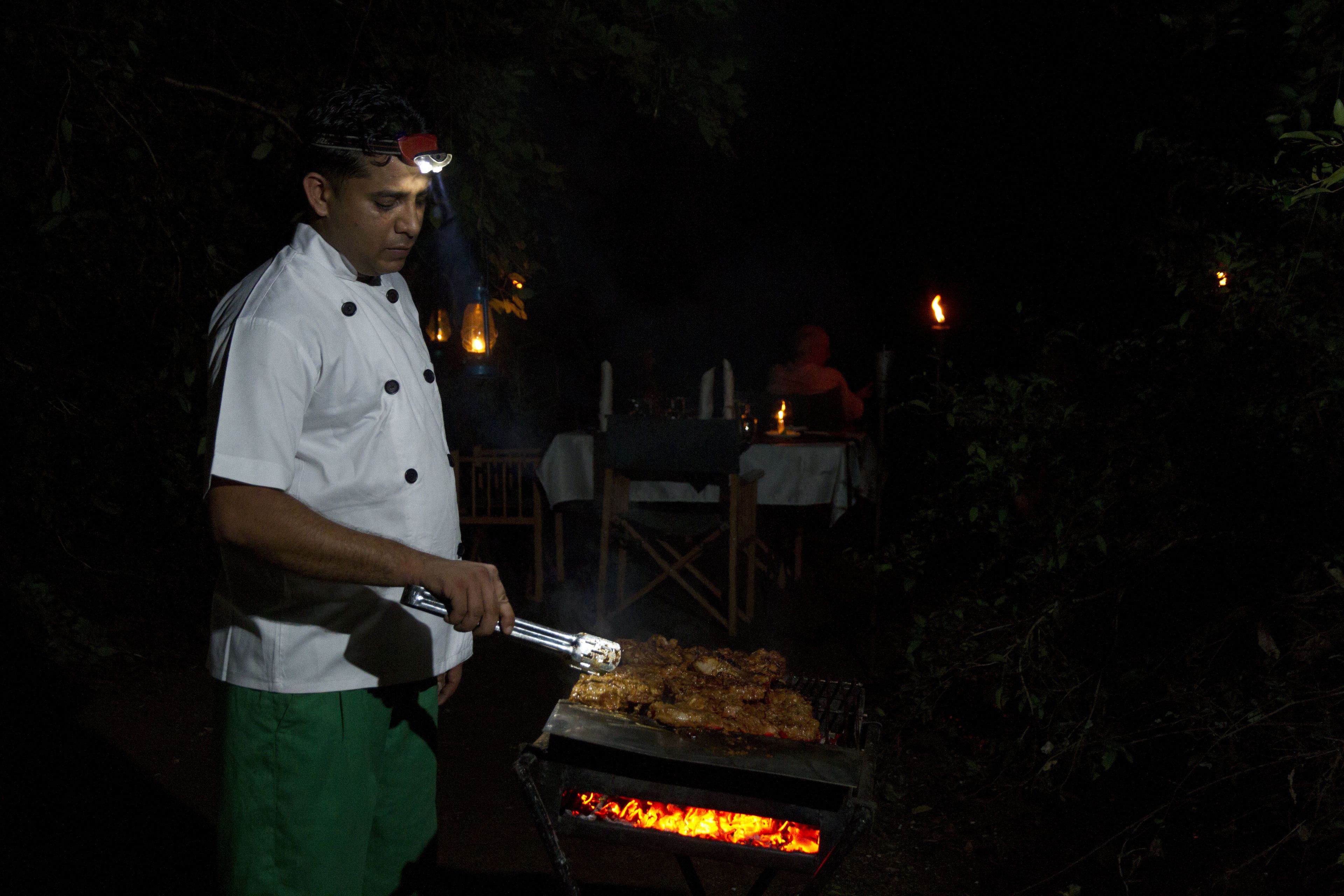 Un chef asando alimentos al aire libre de noche.