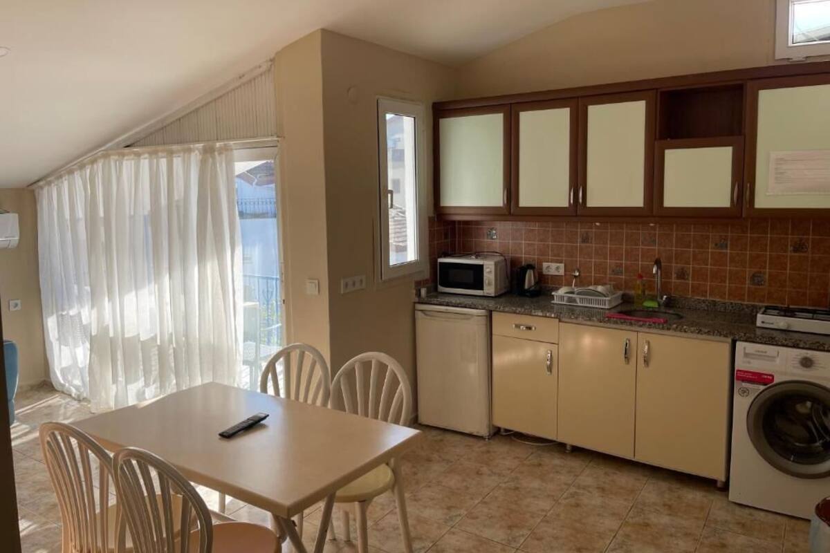 Una cocina compacta con zona de comedor, que incluye una mesa, sillas, microondas, lavadora y armarios.