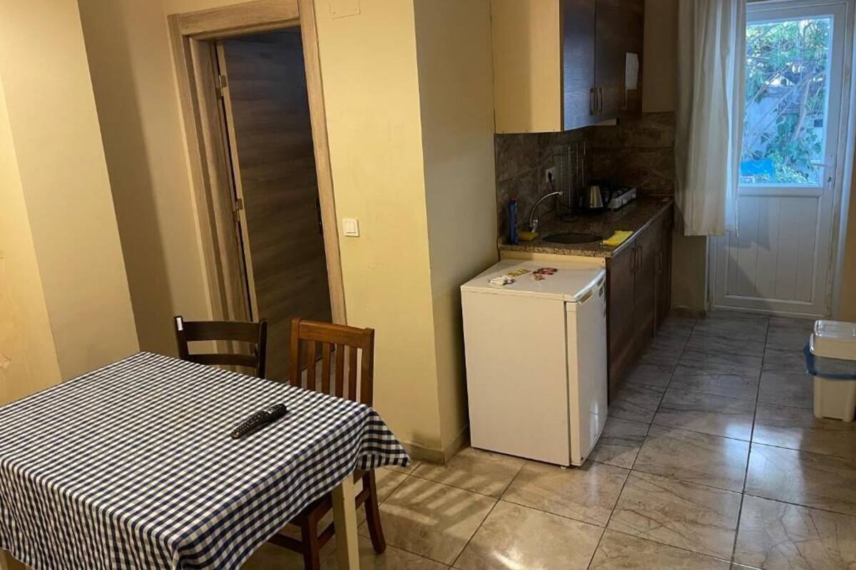 Una cocina compacta con refrigerador, lavamanos y armarios. Hay una mesa de comedor con mantel a cuadros y sillas.