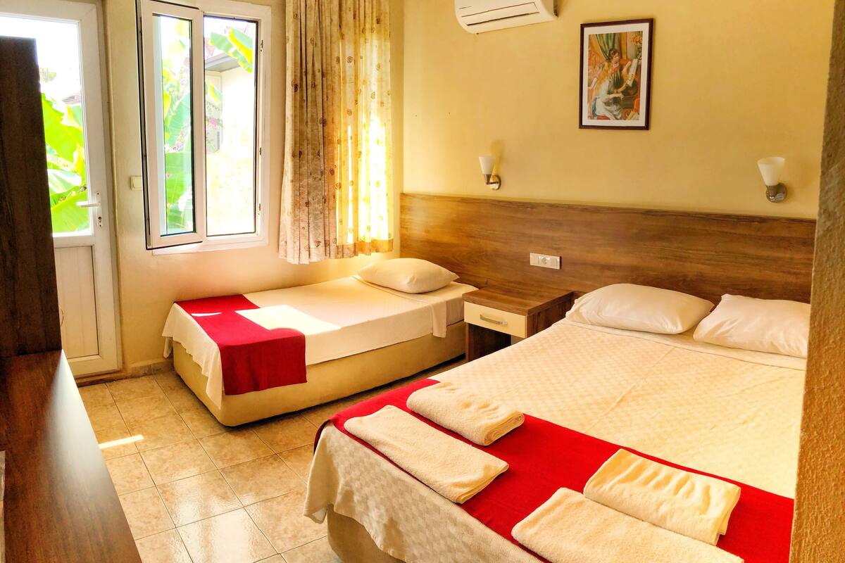 Habitación de hotel con dos camas, una ventana con cortinas, un aire acondicionado y un cuadro en la pared.