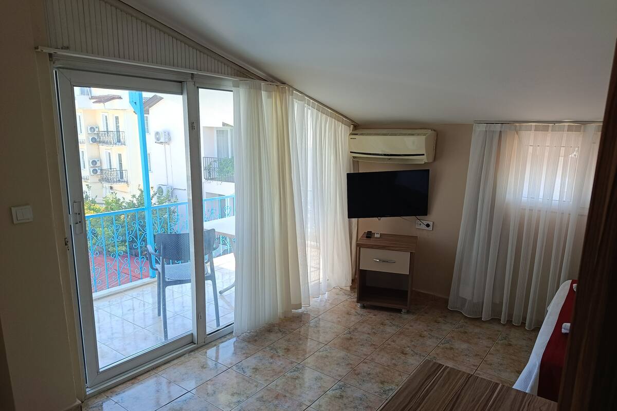 Una habitación con una puerta corrediza de vidrio que da a un balcón, un televisor de pantalla plana montado en la pared y un pequeño armario de madera.