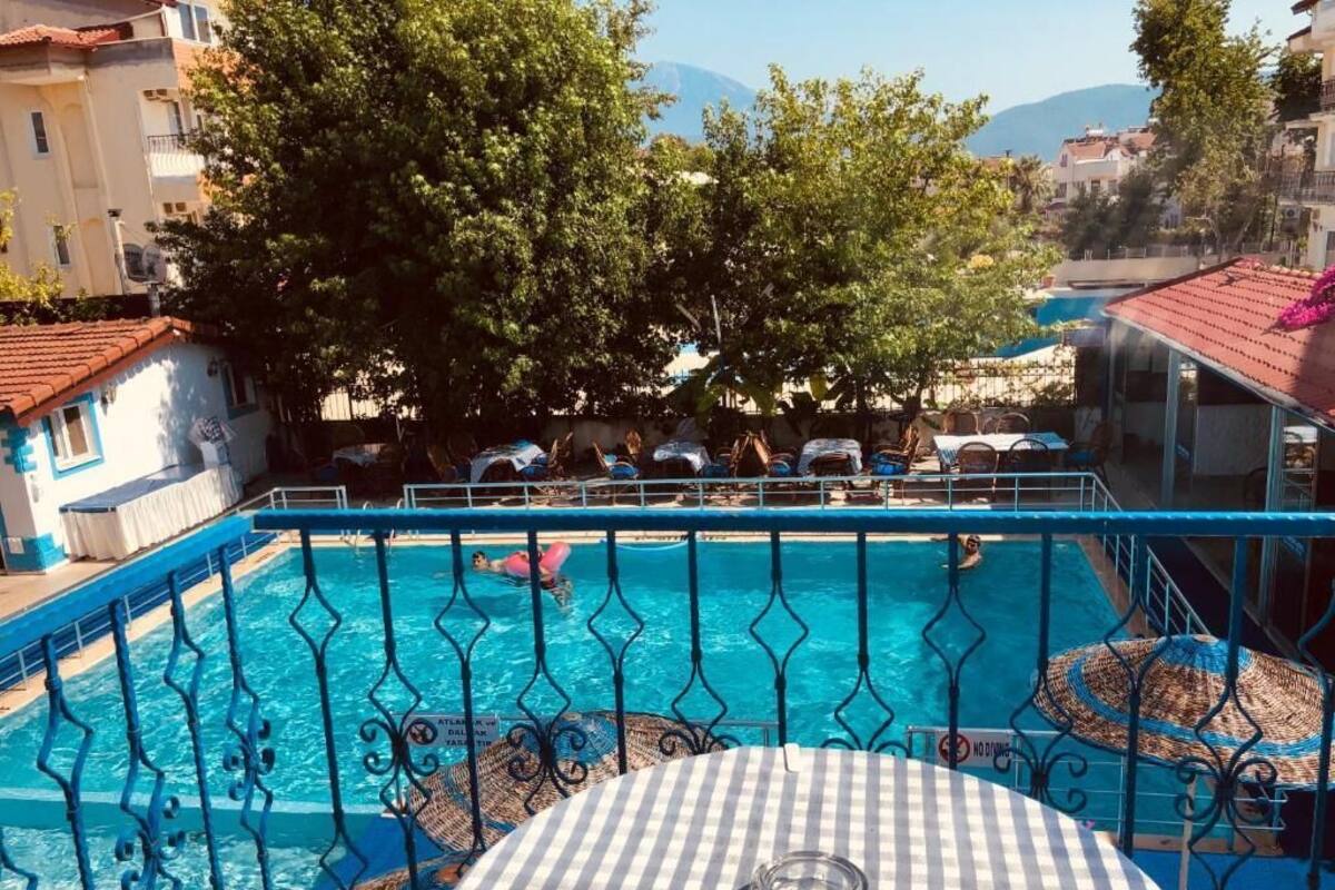 Zona de piscina con una mesa y sillas a cuadros, rodeada por una valla metálica.