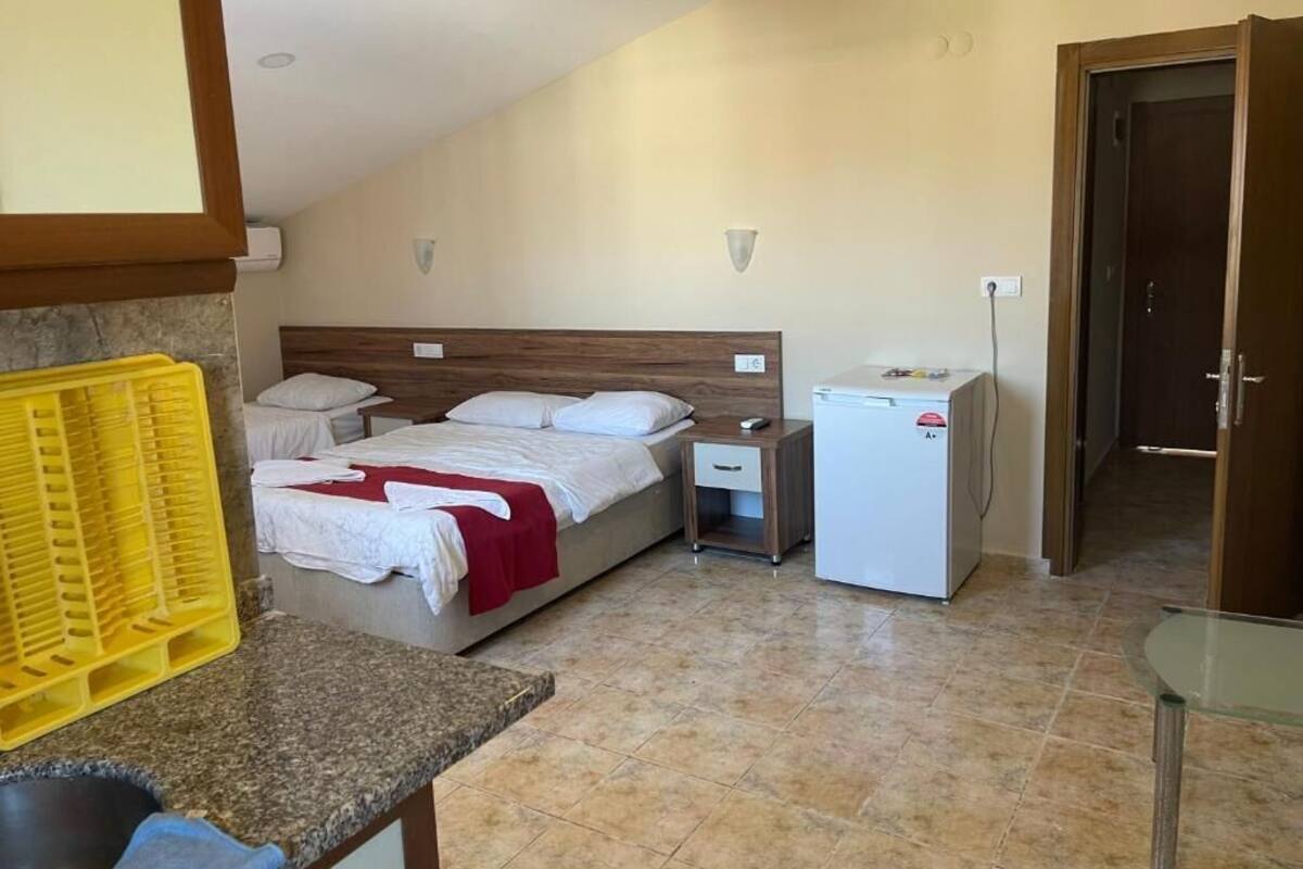 Un dormitorio con cama, una mesita de noche pequeña, un refrigerador y un baño visible a través de una puerta abierta.