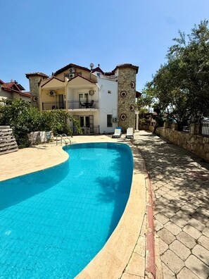 Uma casa de dois andares com piscina, paredes de pedra e varanda.