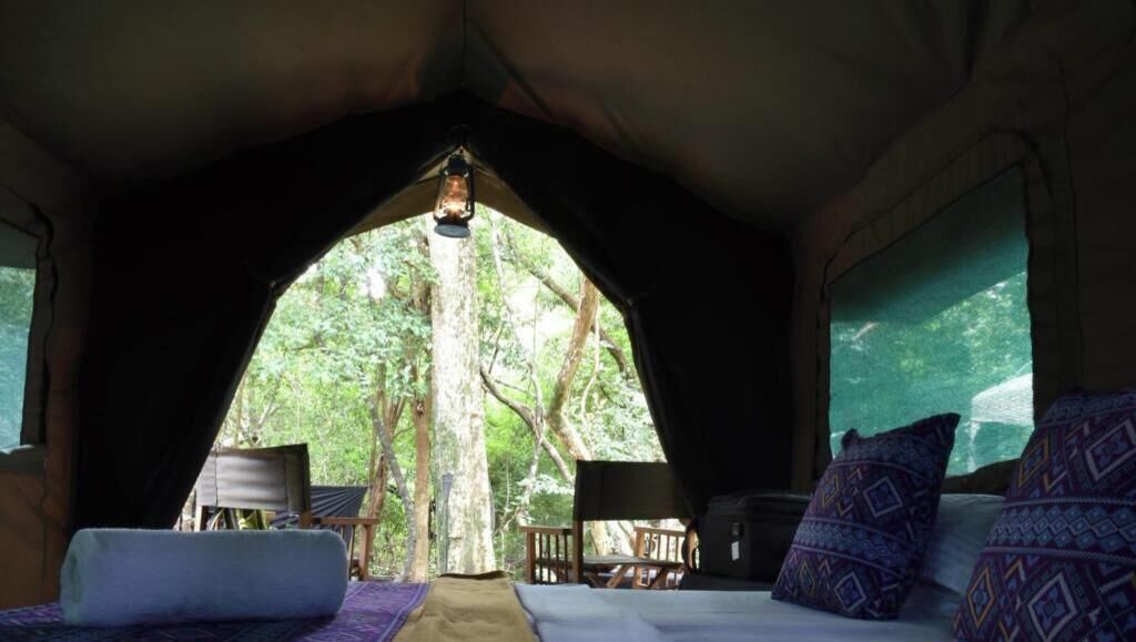 A tent with a bed, pillows, and a table with a lantern.