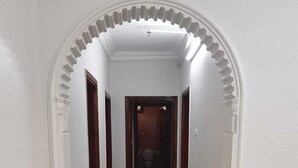 A hallway with a tiled floor, white walls, and an arched doorway leading to a room with a toilet. - AL EAIRY SERVICED APARTMENTS 3 (Madinah)