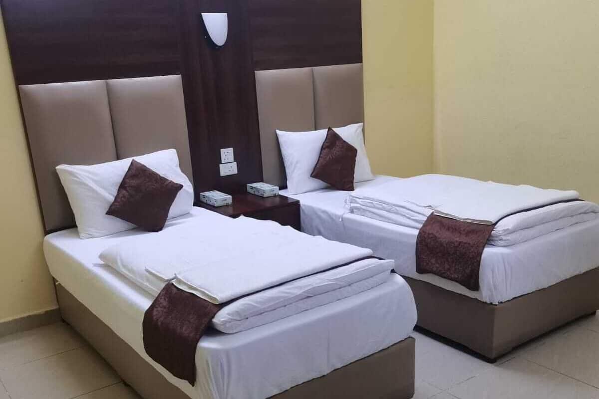 A hotel room with two beds, each with white linens and brown throw pillows.