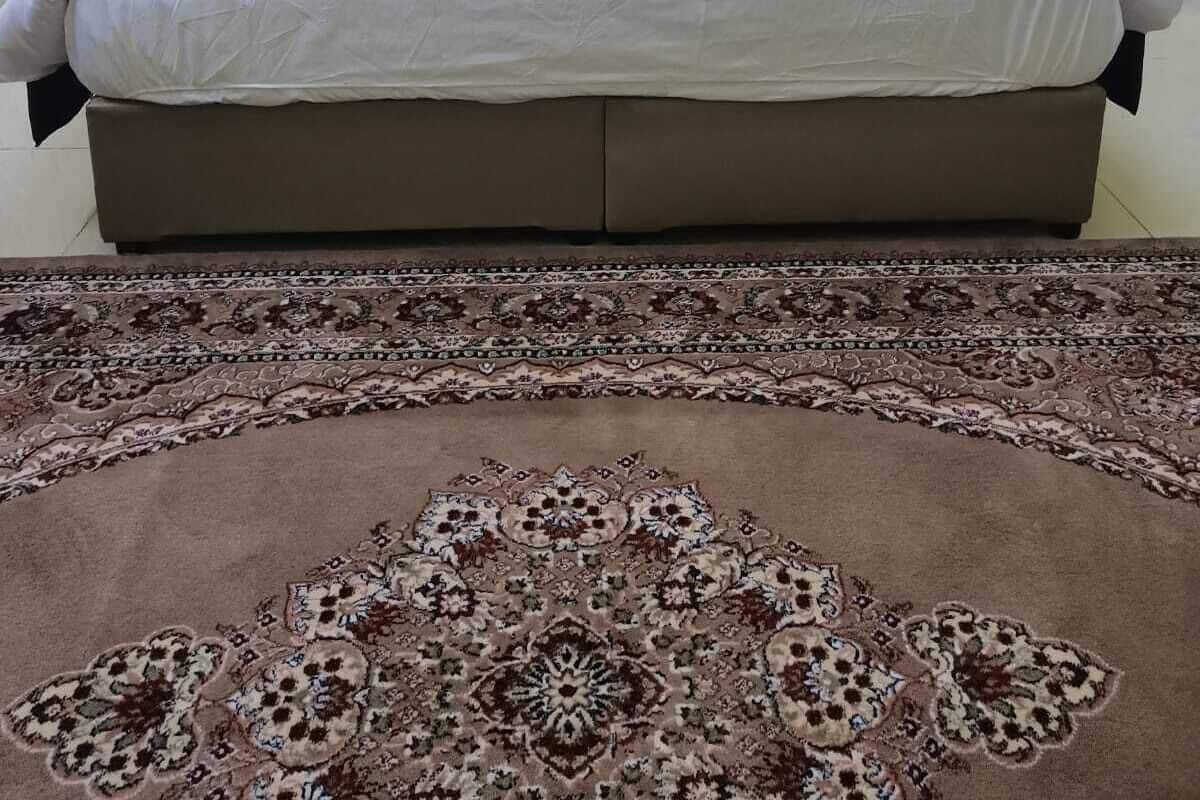 A neatly made bed with a headboard, two bedside tables with lamps, and a patterned carpet.