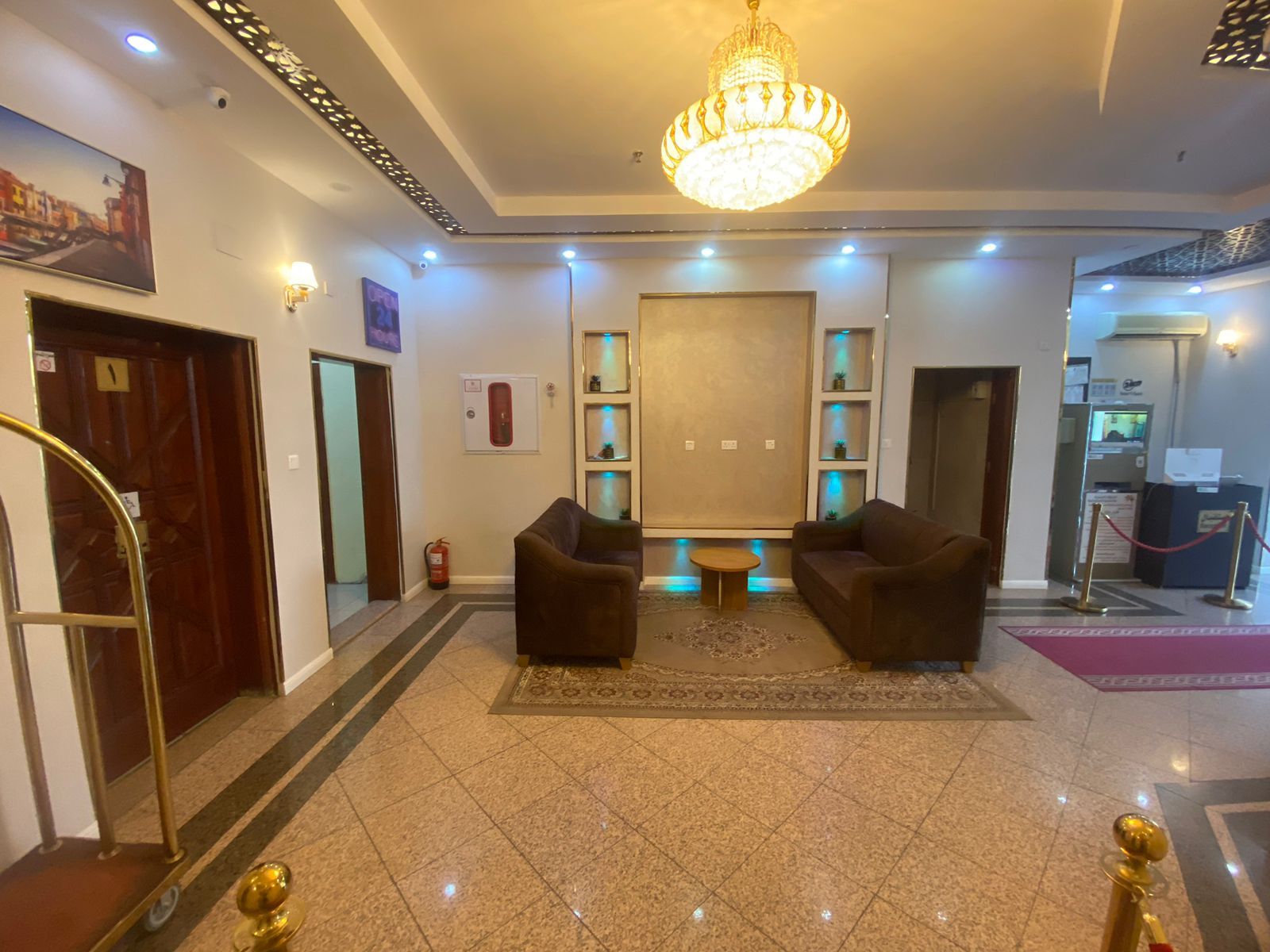 A hotel lobby with a chandelier, two sofas, a reception desk, and a fire extinguisher.