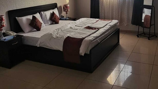 A neatly made bed with a dark headboard, a bedside table with a lamp, and a mirror on a stand. - AL EAIRY SERVICED APARTMENTS 3 (Madinah)