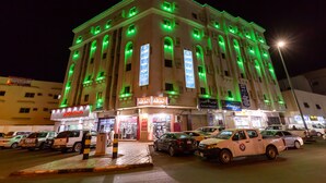 A multi-story building with illuminated signage and multiple ground-level shops. - AL EAIRY SERVICED APARTMENTS 3 (Madinah)