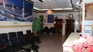 A lobby with a large poster of a mosque, a reception desk with a vase of flowers, and a potted plant. - AL EAIRY SERVICED APARTMENTS 3 (Madinah)