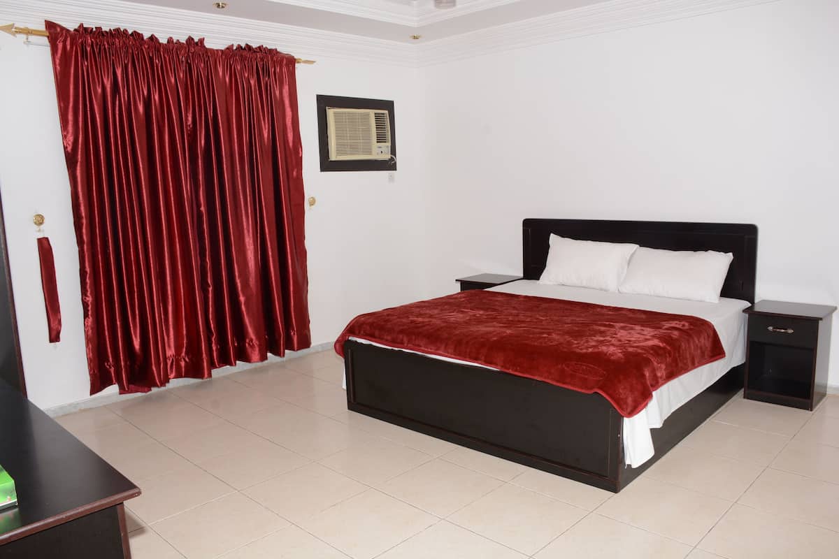 A bedroom with a bed, nightstands, a red curtain, and an air conditioning unit.