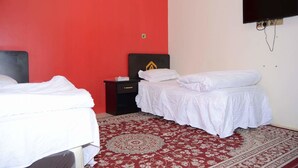 Een hotelkamer met twee bedden, een rode wand, een kamerbreed tapijt en een aan de muur bevestigde televisie.
