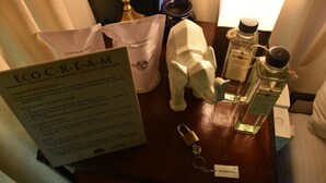 Habitación de hotel con una mesa de madera que muestra un cartel, una figurita blanca y dos botellas de perfume.