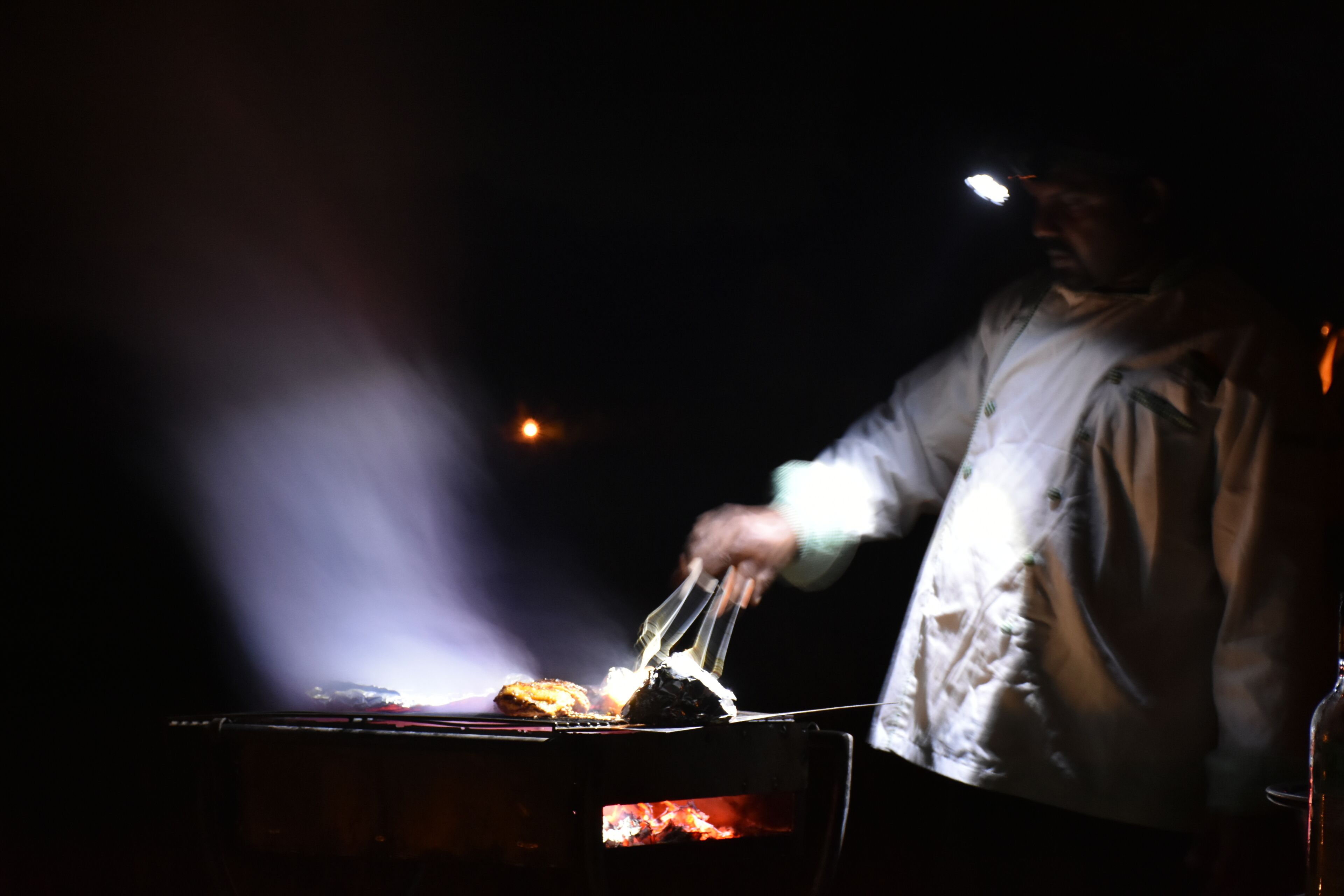 A person grilling food outdoors at night.