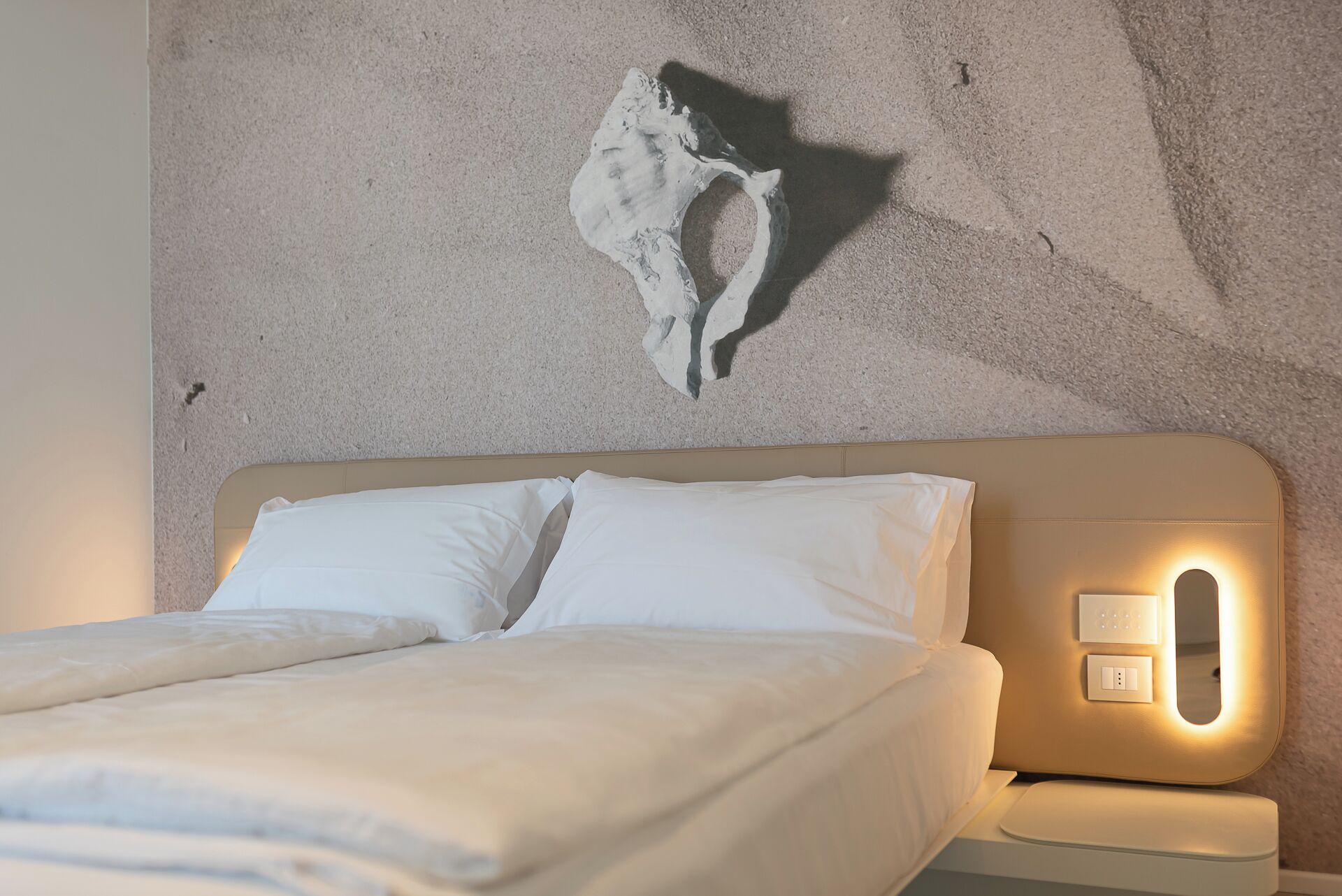 Ein Bett mit weißer Bettwäsche, einem Kopfteil und einer Wandleuchte.