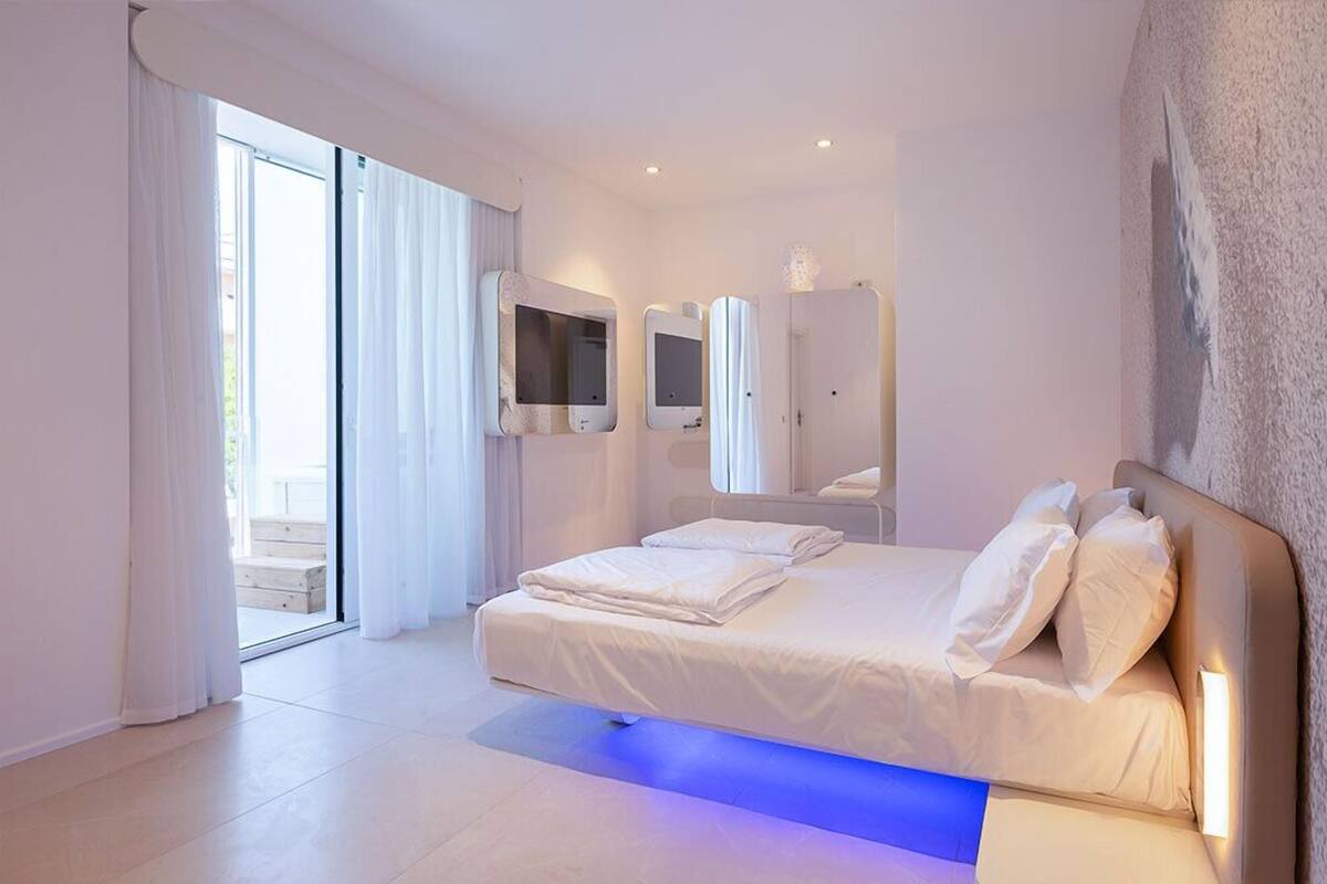 A modern bedroom with a large bed, sliding glass doors leading to a balcony, and built-in wall mirrors.