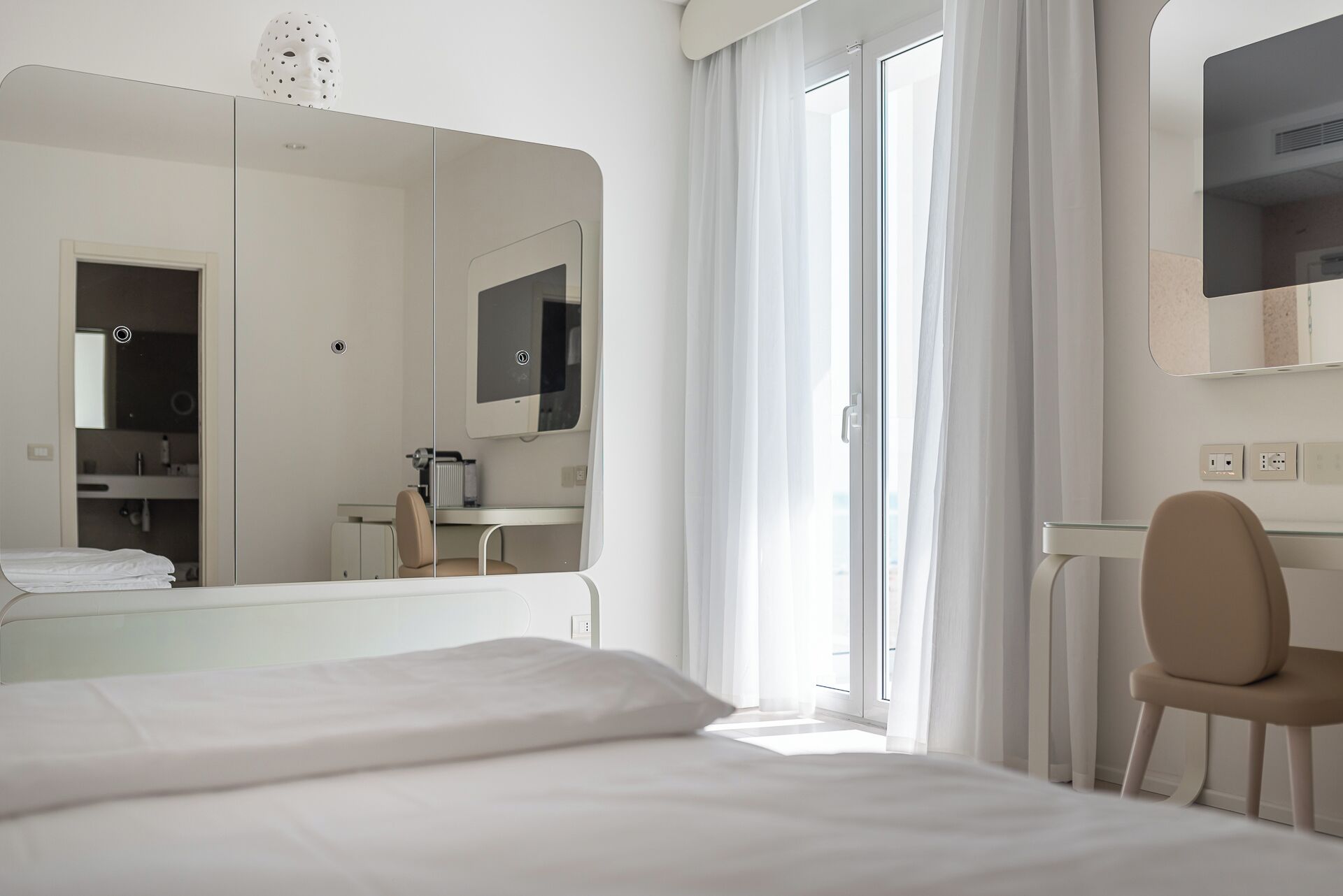 Una habitación de hotel moderna con una cama grande, una silla, un escritorio, un espejo y una ventana con cortinas.