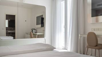 A modern hotel room with a large bed, a chair, a desk, a mirror, and a window with curtains.