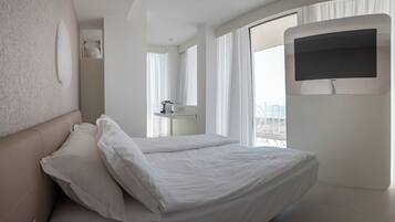 Une chambre d’hôtel moderne, équipée d’un lit, d’un téléviseur fixé au mur et offrant une vue sur la plage.