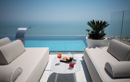 A rooftop terrace with a pool, two sofas, a table with drinks, and a potted plant.