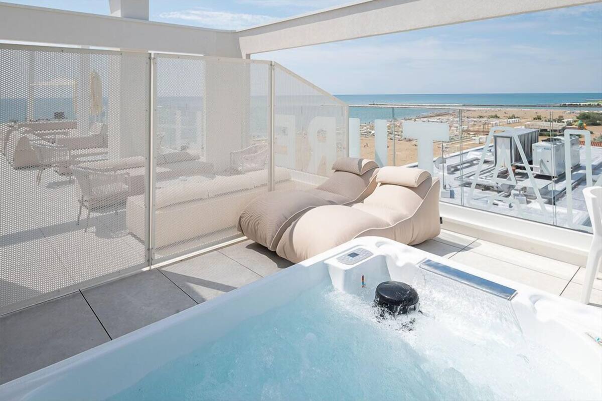 A rooftop terrace with a hot tub, lounge chairs, and a view of the beach.