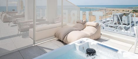 A rooftop terrace with a hot tub, lounge chairs, and a view of the beach.
