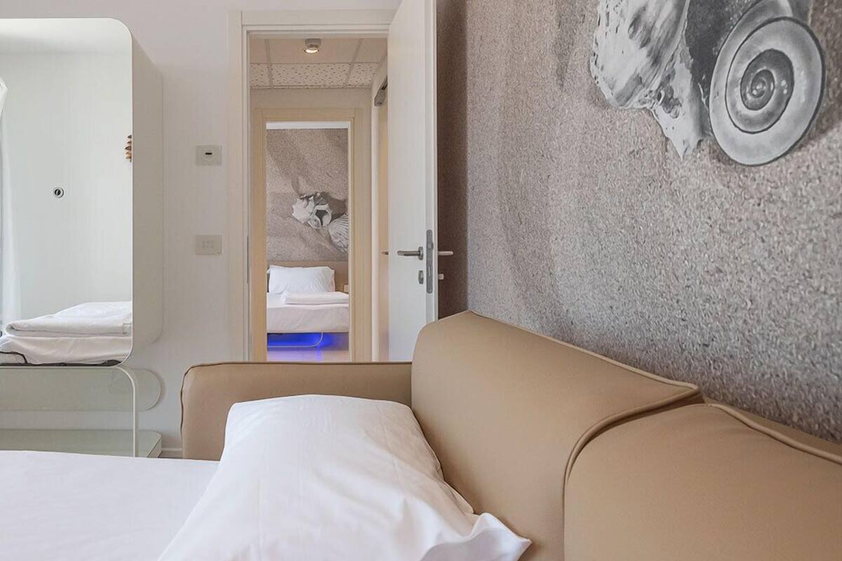 A hotel room with a bed, a sofa, a door leading to a bathroom, and a wall with a textured design.